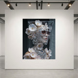 A surreal fashion portrait of a model with sleek platinum blonde hair, smokey sunglasses, diamond necklace and matching diamond face mask adorned with delicate pink flowers set against a dark background displayed on a large white gallery wall in a luxurious acrylic glass frame.