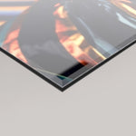 A close-up angled view of a 4mm glossy acrylic glass panel with a dark reflective surface showing warm orange and blue tones, set against a light grey background.