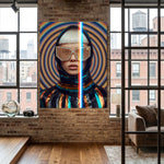 A large vertical canvas print featuring a stylized portrait of a woman with a platinum blonde bob, gold geometric sunglasses, and a metallic reflective outfit, displayed on a brick wall in a modern loft room with wood floors and large windows. 