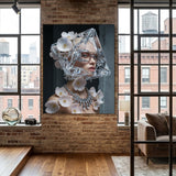 A large framed wall art print hangs on a brick wall in a modern loft-style room with wood floors and large windows. The artwork shows a woman's face and neck adorned with pink flowers, a clear geometric headpiece and a silver diamond necklace against a dark background.