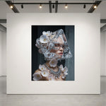 A large framed art print displayed on a white gallery wall, featuring a surreal portrait of a woman wearing a clear geometric crystal-like headpiece with pink flowers and a silver diamond necklace against a dark background. 