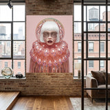 A large vertical wall art under acrylic glass featuring a stylized portrait of a woman with white hair and a pink bubble-like collar, displayed on a brick wall in a modern loft interior with windows and a sofa visible. 