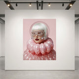 A large artwork displayed on a white gallery wall, featuring a stylized portrait of a woman with white hair, glittery mask, and voluminous pink ruffled glass clothing against a pink background. 