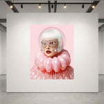 A large artwork displayed on a white gallery wall, featuring a stylized portrait of a woman with white hair, glittery mask, and voluminous pink ruffled glass clothing against a pink background. 