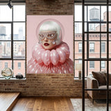 A large vertical wall art featuring a stylized portrait of a woman with a pink bubble helmet and voluminous pink ruffled clothing, displayed on a brick wall in a modern loft room with wood floors and large windows.