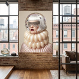 A large framed wall art hangs on a brick wall in a loft-style room with wood floors and large windows. The artwork depicts a surreal portrait of a woman wearing a reflective clear space helmet and a voluminous cream ruffled collar against a pale background. 