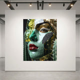 A large square art print depicting a stylized close-up portrait of a woman's face with green and gold textures, red lips, and black diamond cheek detail, displayed on a white gallery wall in a modern gallery space with track lighting. 