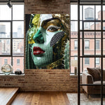 A large wall surreal artwork featuring a stylized close-up portrait of a woman's face with green, gold, and black mask-like elements and red lips, displayed on a brick wall in a modern loft interior with windows and wood flooring.