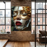 A large wall artwork featuring a close-up of a face in a metallic gold mask with red lips and a gold rose, displayed on a brick wall in a modern loft-style room with wood floors and windows.