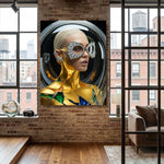 A large framed wall art featuring a stylized portrait of a woman wearing metallic gold and silver futuristic diamond eyewear, earrings and ear cuff. Her body is covered in gold with sapphires and emeralds accents. Scene is displayed on a brick wall in a modern loft interior with wood floors and large windows. 