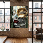 A large canvas wall art print featuring a stylized, transparent acrylic face with gold, silver, and red details, set in a cacti decor, displayed on a brick wall in a modern loft-style room with wood floors and windows.