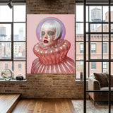A large vertical artwork displayed in an acrylic glass frame featuring a stylized portrait of a woman with platinum white hair, a pink background, and a glossy pink ruffled collar, displayed on a brick wall in a modern loft room with windows and a sofa.