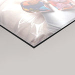 A close-up of a glossy, transparent acrylic or glass panel with a black edge, reflecting light and showing a colorful abstract painting in the background.