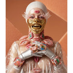 A person wearing a white head covering, a gold face mask, silver gloves, and a clear plastic jacket, with multiple pink lips attached or styled on the face, neck, and chest, posed against a peach-colored textured background. 