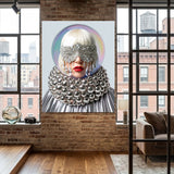 A large vertical wall art print featuring a stylized portrait of a woman with silver eye masks, a voluminous silver collar, and white hair, displayed on a brick wall in a modern loft room with wood floors and windows.