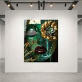 A square wall-mounted artwork in a gallery setting, featuring a surreal still life with a green glass face, gold-toned succulent and flower elements, a dark red lips motif. The artwork is displayed on a large white wall under gallery spotlights.