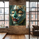 A large wall art print featuring a stylized, geometric face in green, gold, and red tones, displayed on a brick wall in a modern loft-style room with wood floors and large windows. 
