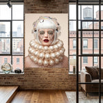 A large wall art depicting a stylized portrait of a woman with white hair, pearl-like ruffs collar, crystal tear droplets, and red lips displayed on a brick wall in a modern loft-style room with windows and a sofa.
